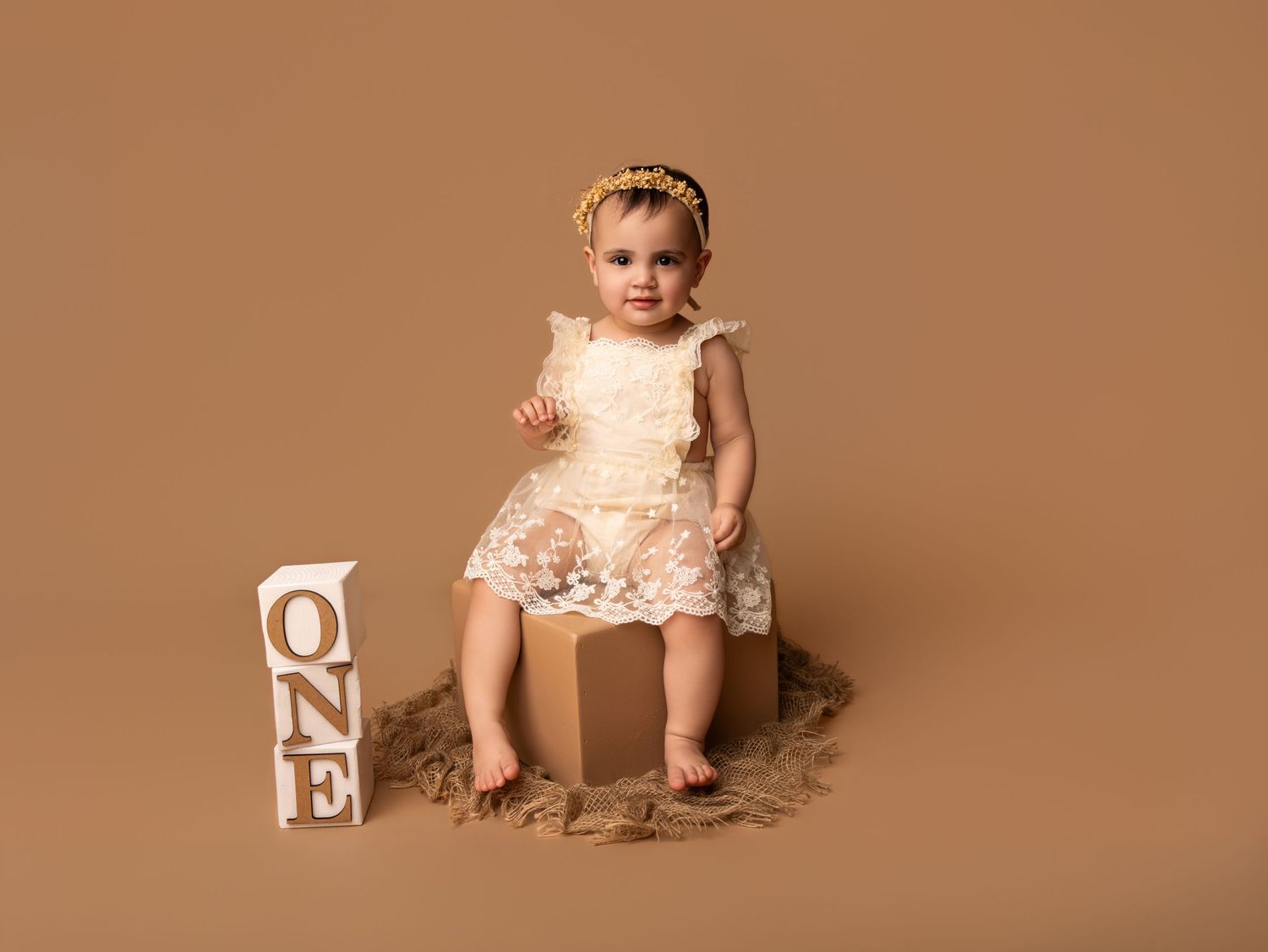 A surprised 6 month old baby sitting in a high chair on a white backdrop, covered in chocolate cake.