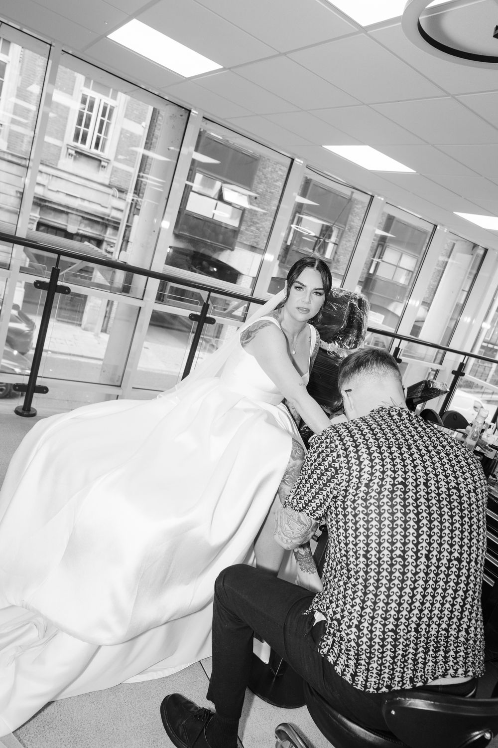 A person in a flowing white dress sits in what appears to be a salon or styling area with mirrored walls and bright lighting.