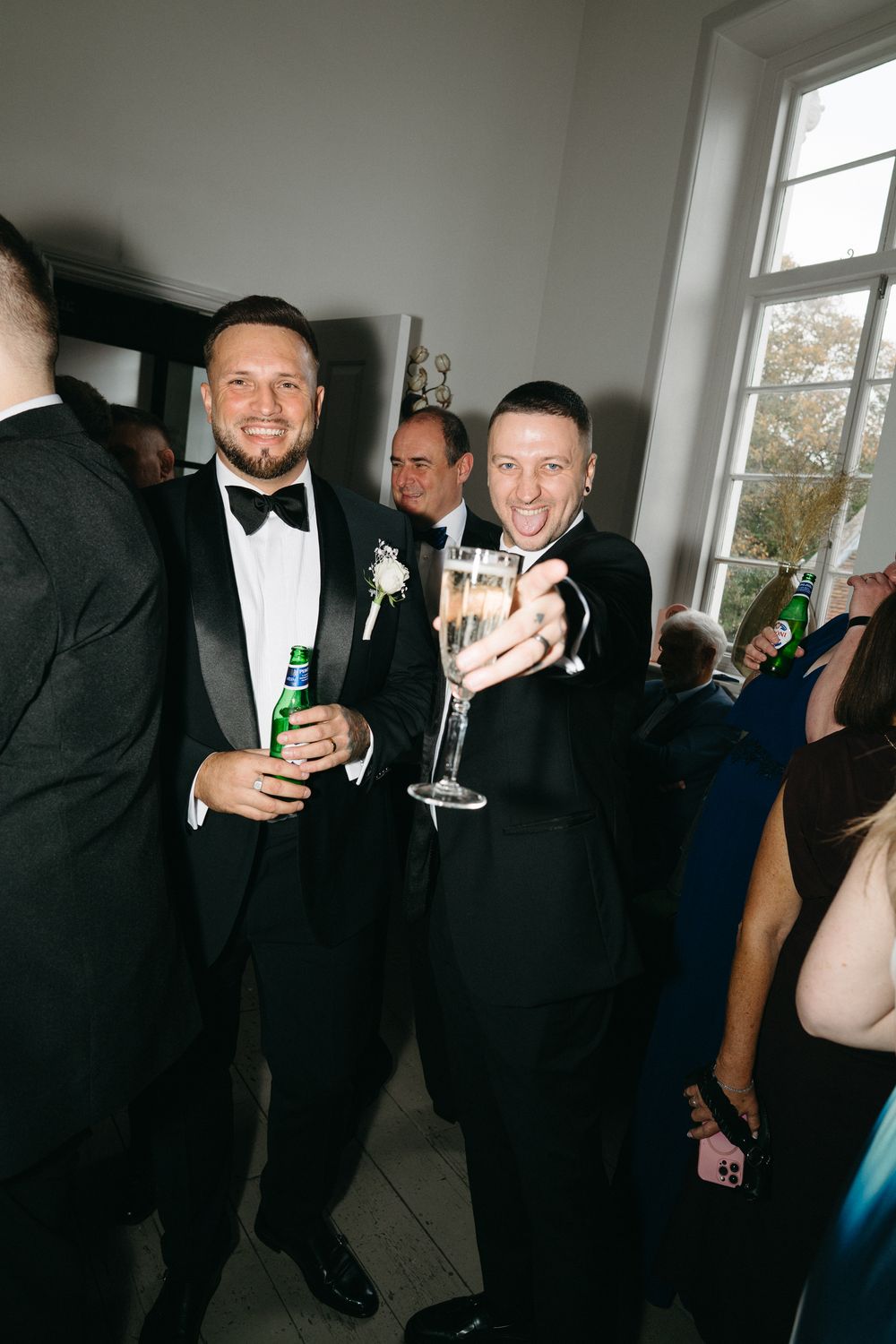 A group of formally dressed guests at a celebration holding drinks and mingling in a bright indoor space.