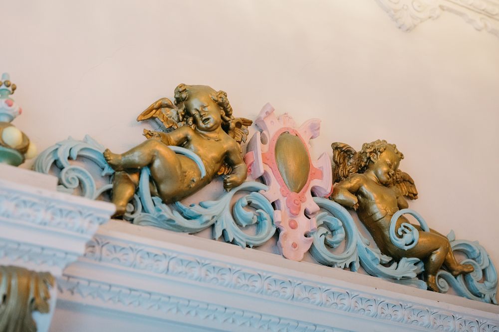 Ornate gold and white decorative crown molding with baroque style flourishes adorns the ceiling of an elegant room.