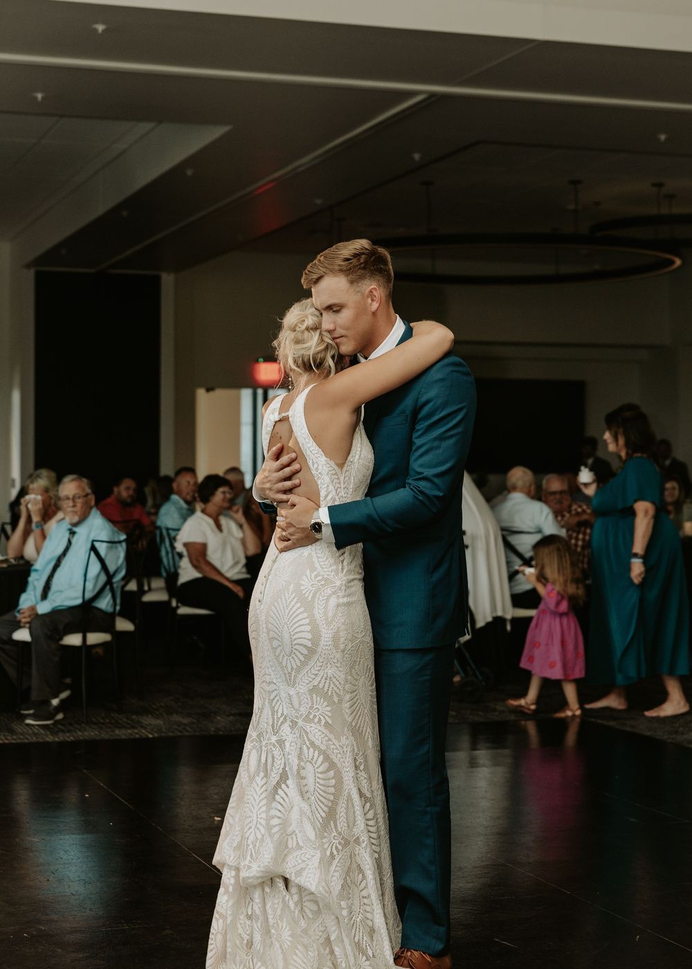 Couples dance together during a wedding reception in a dimly lit venue with guests watching in the background.