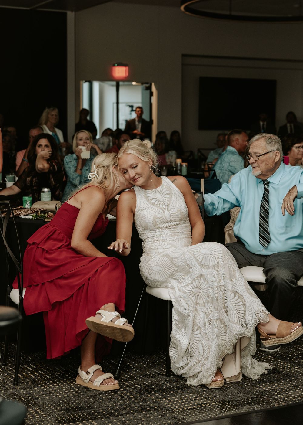 Two wedding guests share a candid laughing moment while seated at a reception table.