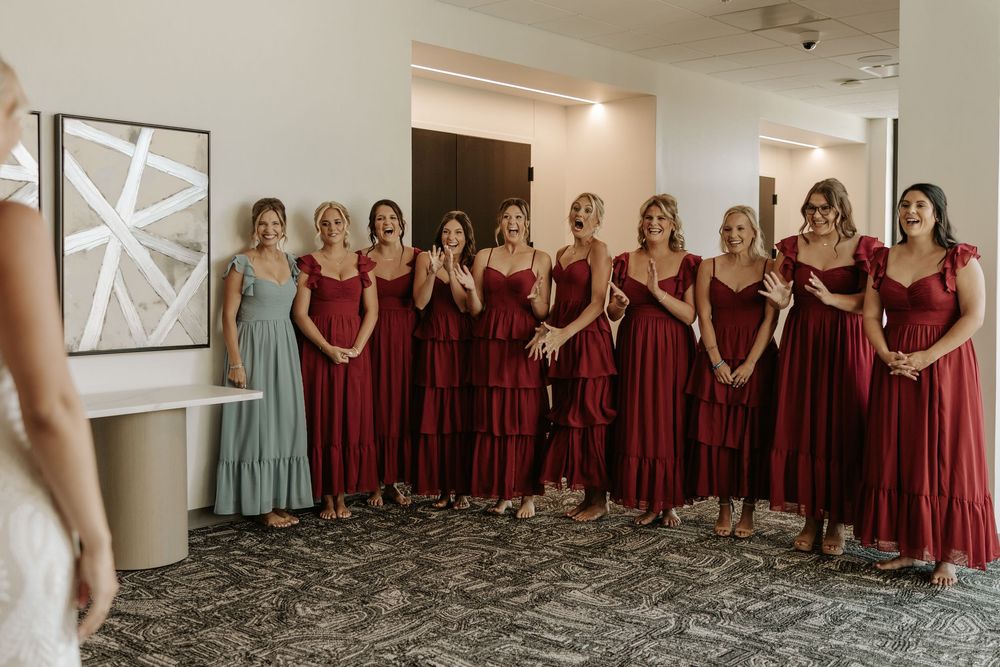 Bridesmaids in burgundy dresses line up against white wall with modern star artwork.