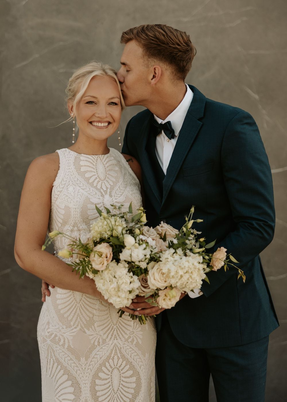 An elegant white bridal bouquet features cream roses and delicate greenery against a grey backdrop.