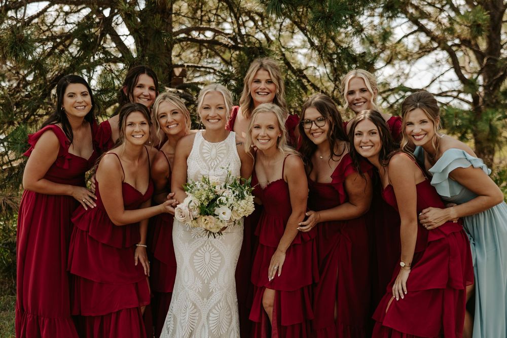 Bridal party in burgundy dresses poses together outdoors for a group photo.