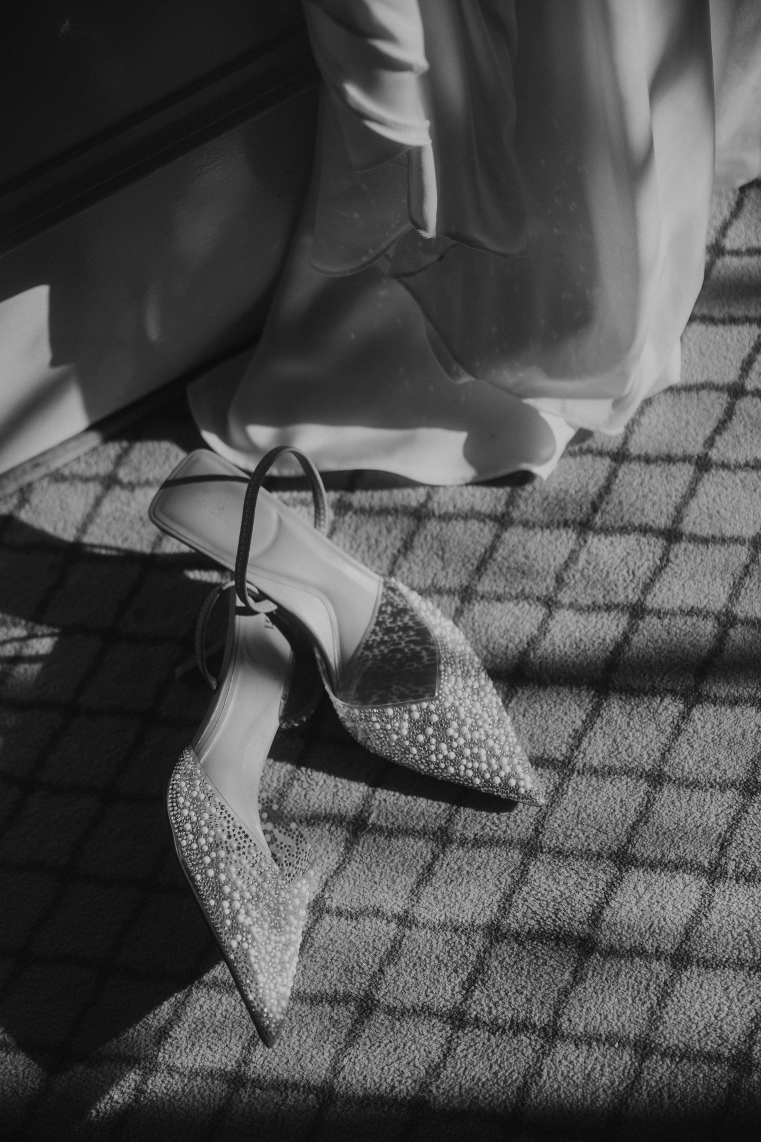 Black and white photo of sparkly high heels on a patterned floor casting dramatic shadows.
