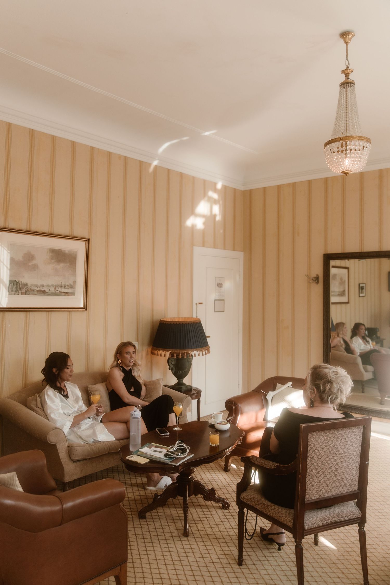 People relax in an elegant hotel suite with cream striped wallpaper, plush seating, and warm lighting.