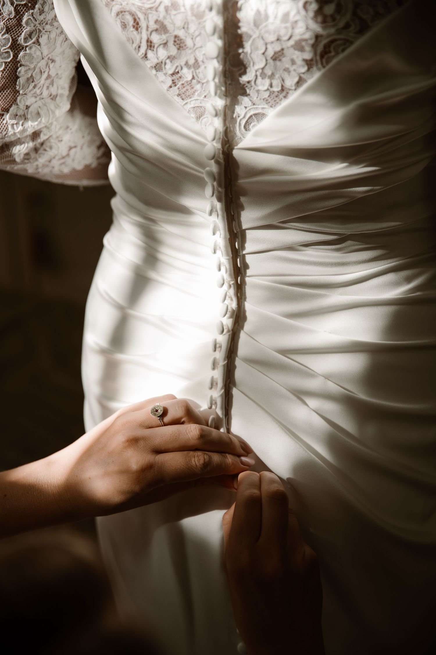 Close-up sequence of hands lacing up the back of an elegant white wedding dress with delicate details.