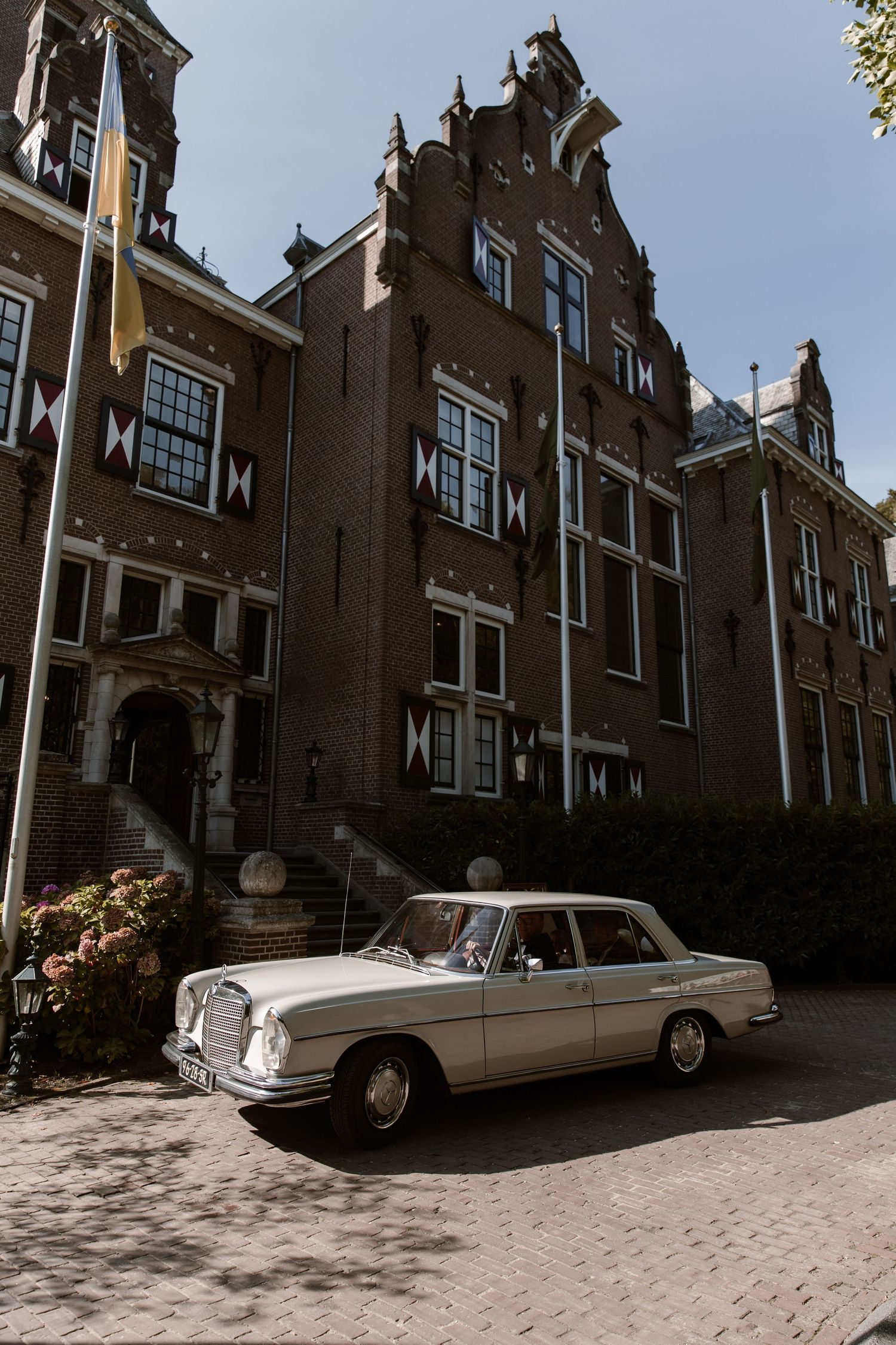 Vintage Mercedes-Benz sedan parked in front of ornate Dutch-style brick building with stepped gable facade.