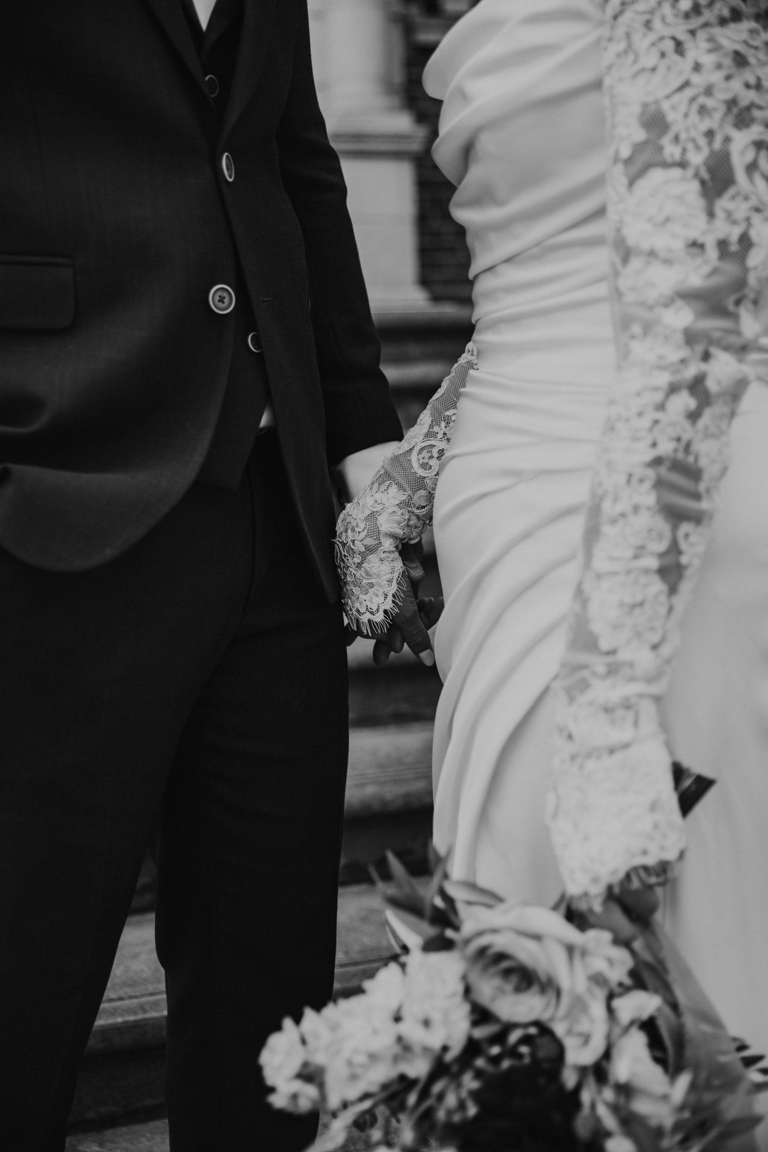 Black and white wedding photo detail showing elegant white bridal gown contrasting with dark formal suit.
