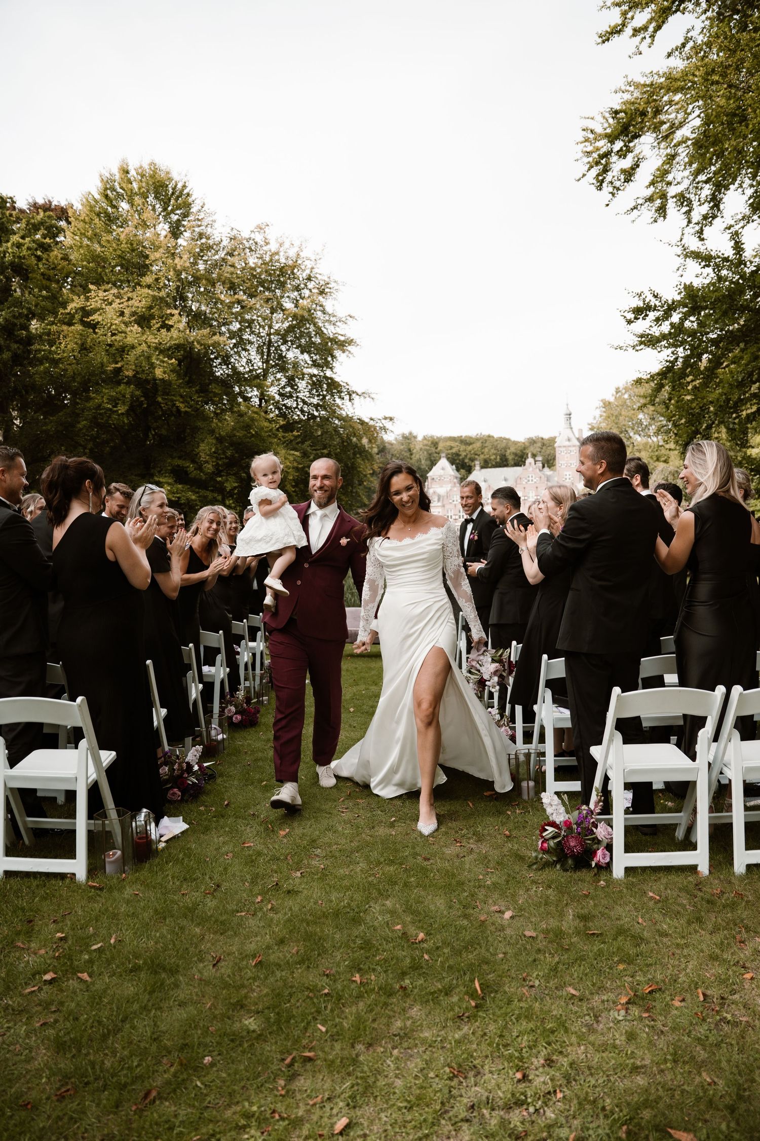 Wedding guests mingle and socialize during an outdoor ceremony with white chairs arranged on a grassy lawn.