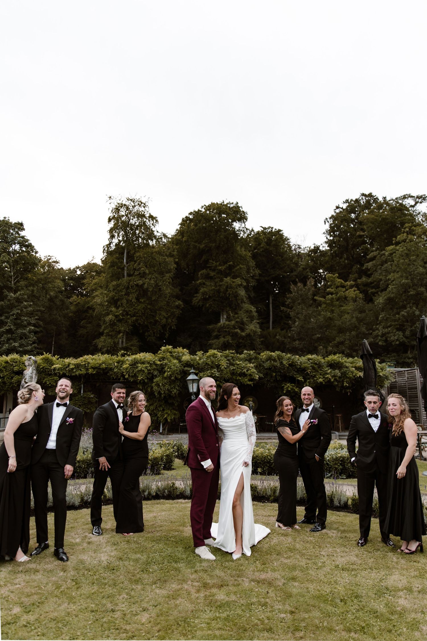 Wedding party guests mingle and socialize on a grassy lawn with trees in the background.