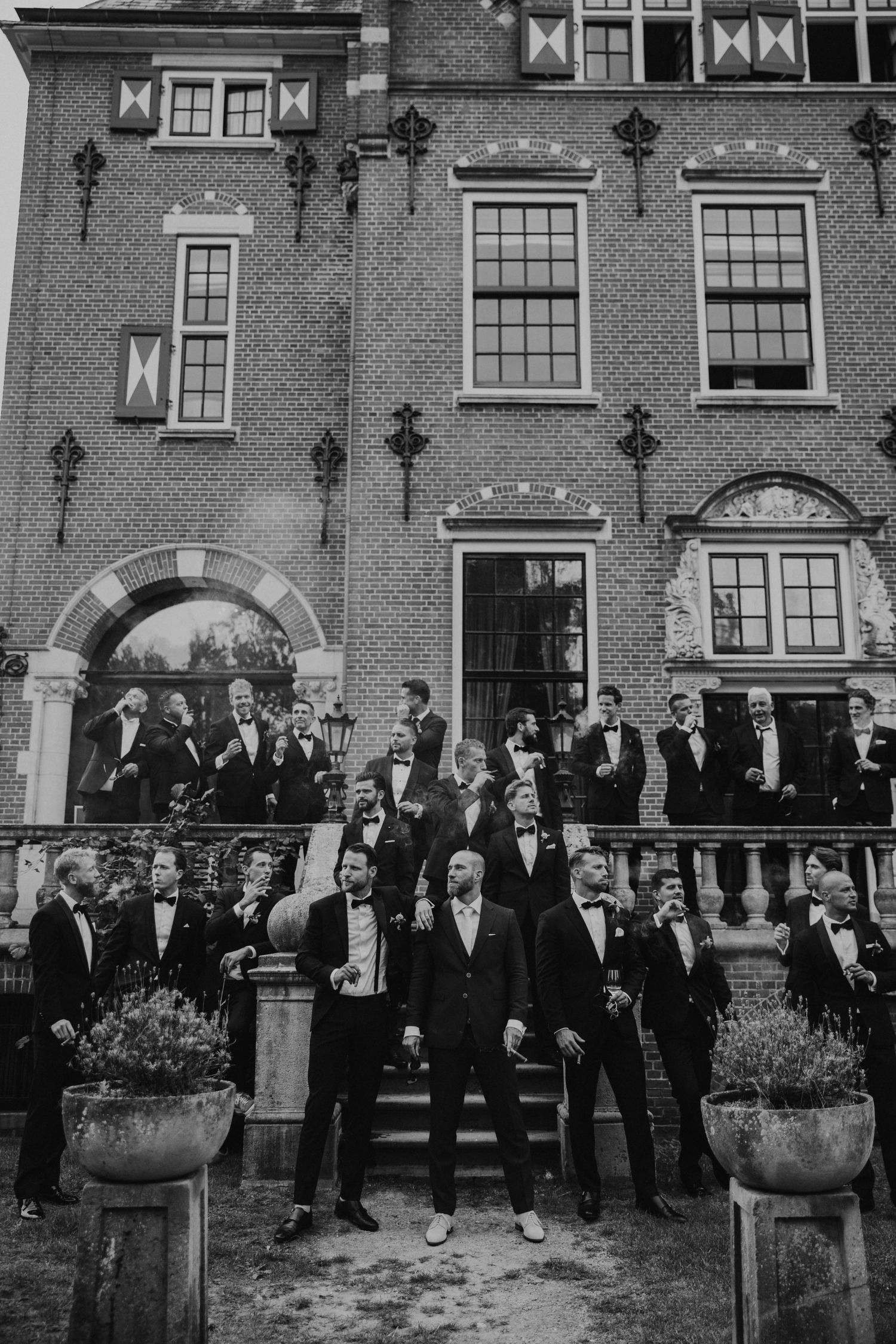 A vintage black and white photograph showing a large group of formally dressed people gathered outside a brick building.