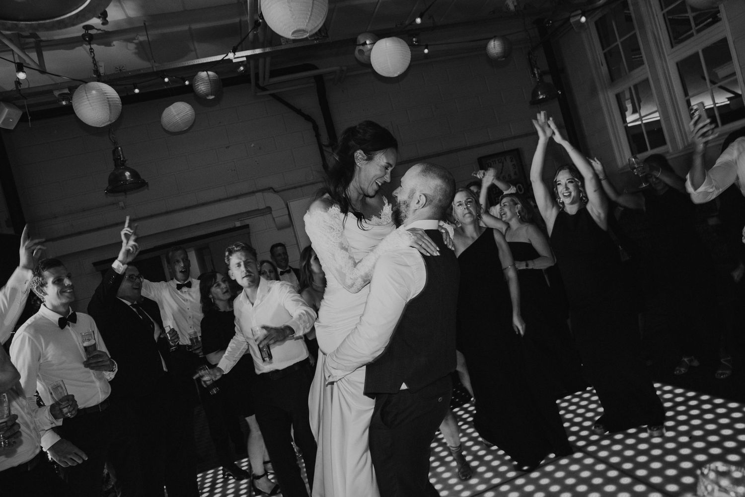 People dancing and celebrating at a lively party with checkered floor and hanging lanterns in a dimly lit venue.