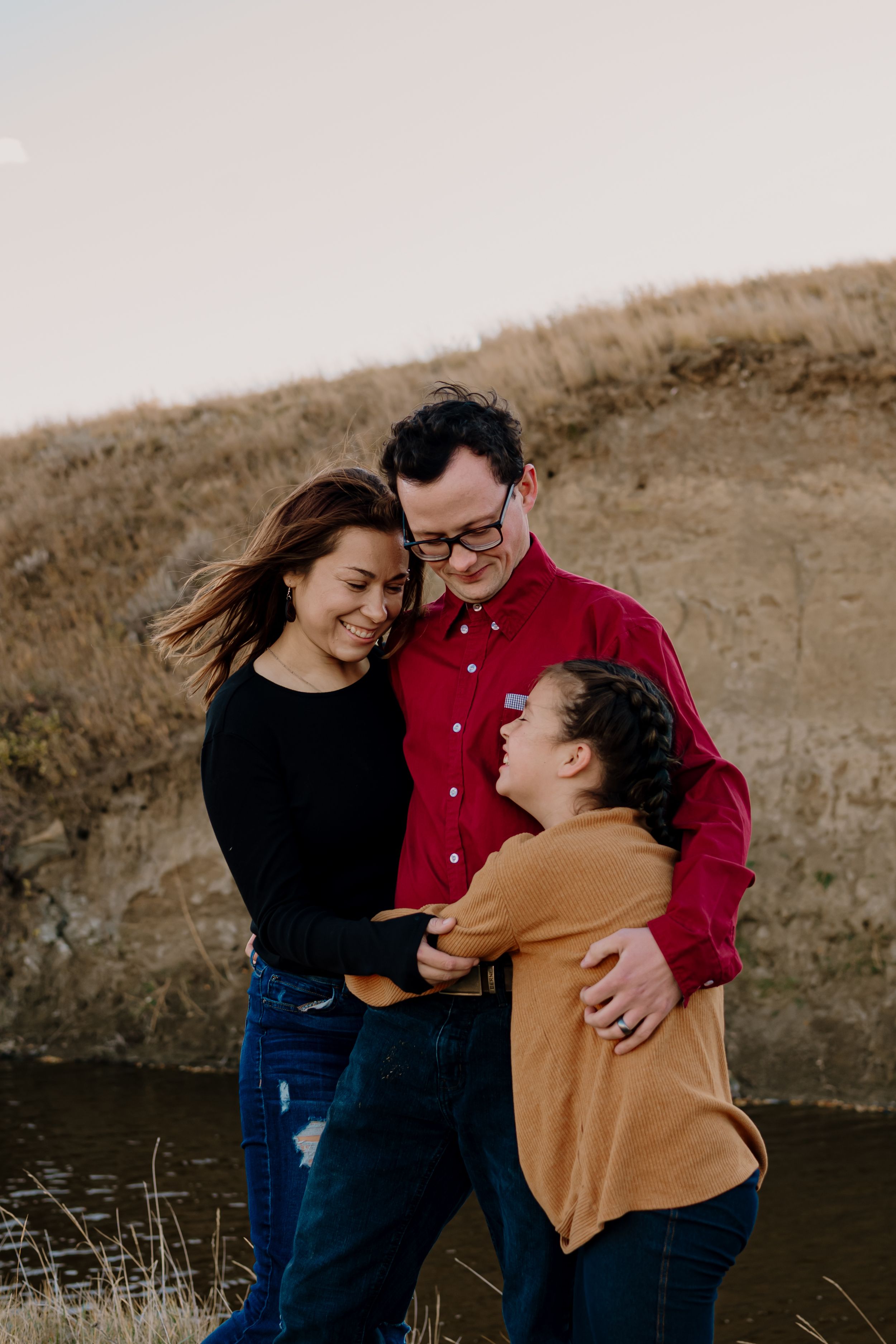A family shares joyful embraces and laughter while posing together in a rustic outdoor setting at sunset.