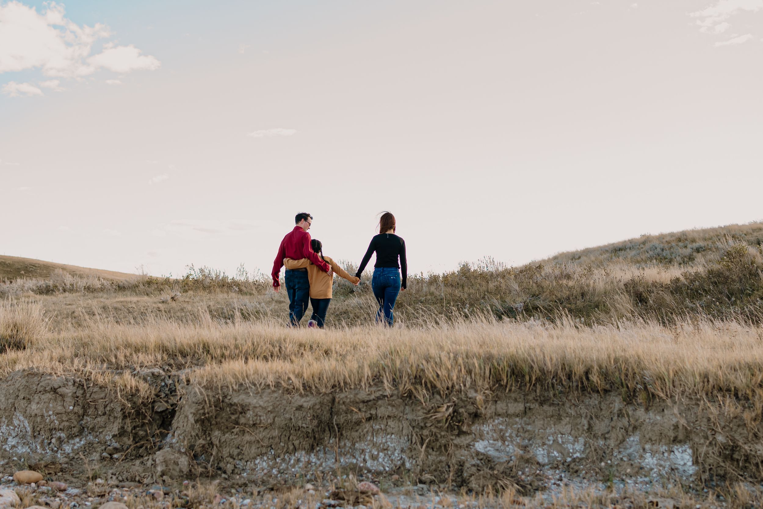 Two people walk together on a grassy hillside path against a cloudy sky at sunset.
