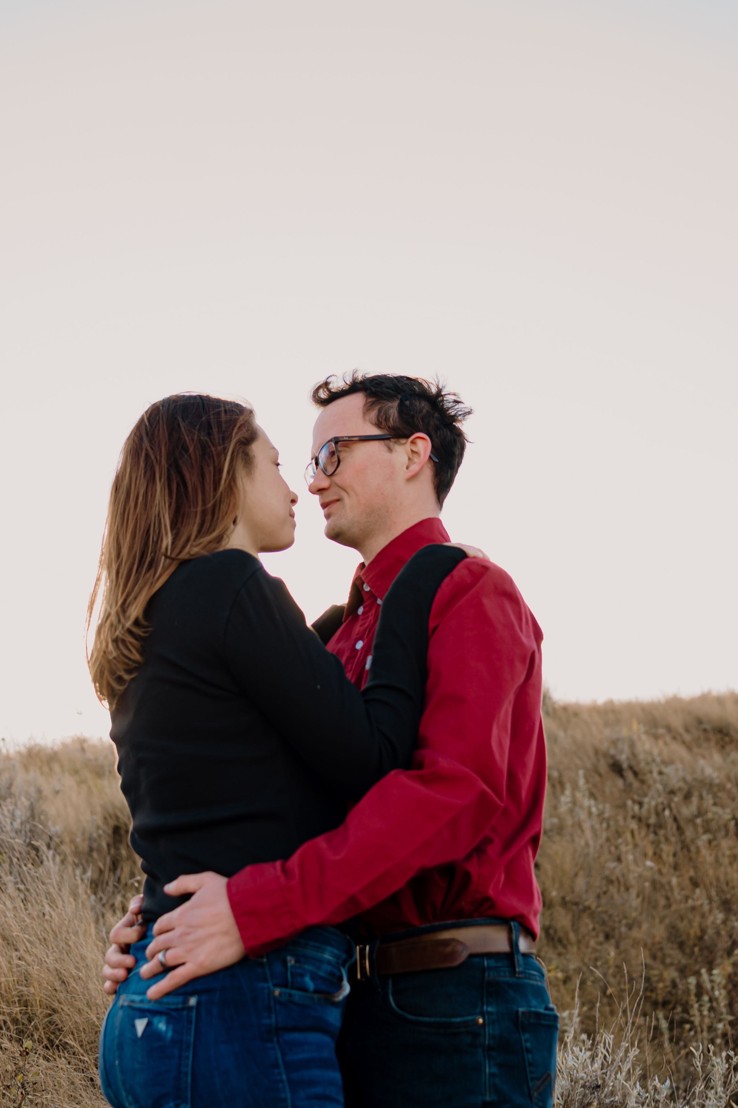 A couple shares intimate moments and embraces against a bright sky backdrop in a natural setting.