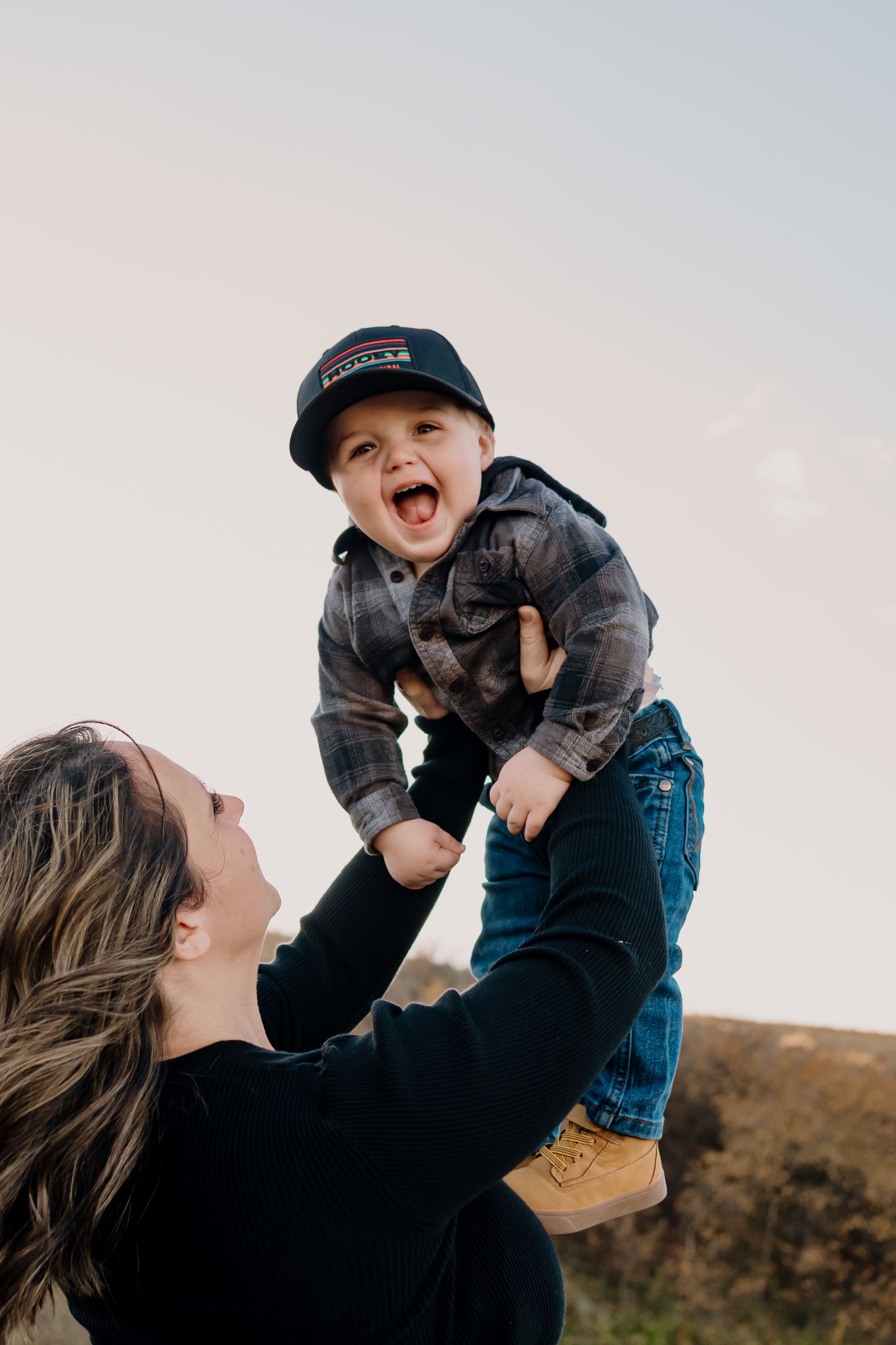 Parent lifts child playfully in the air against a scenic outdoor backdrop during a heartwarming candid moment.