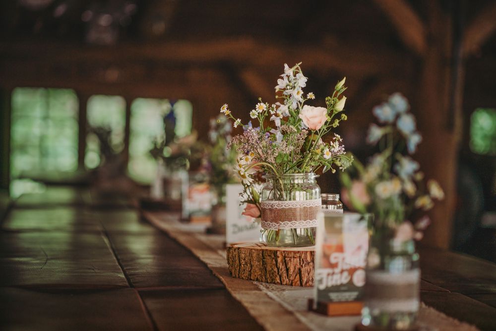 Rustic wedding reception table settings with delicate floral centerpieces and candles in a wooden barn venue.