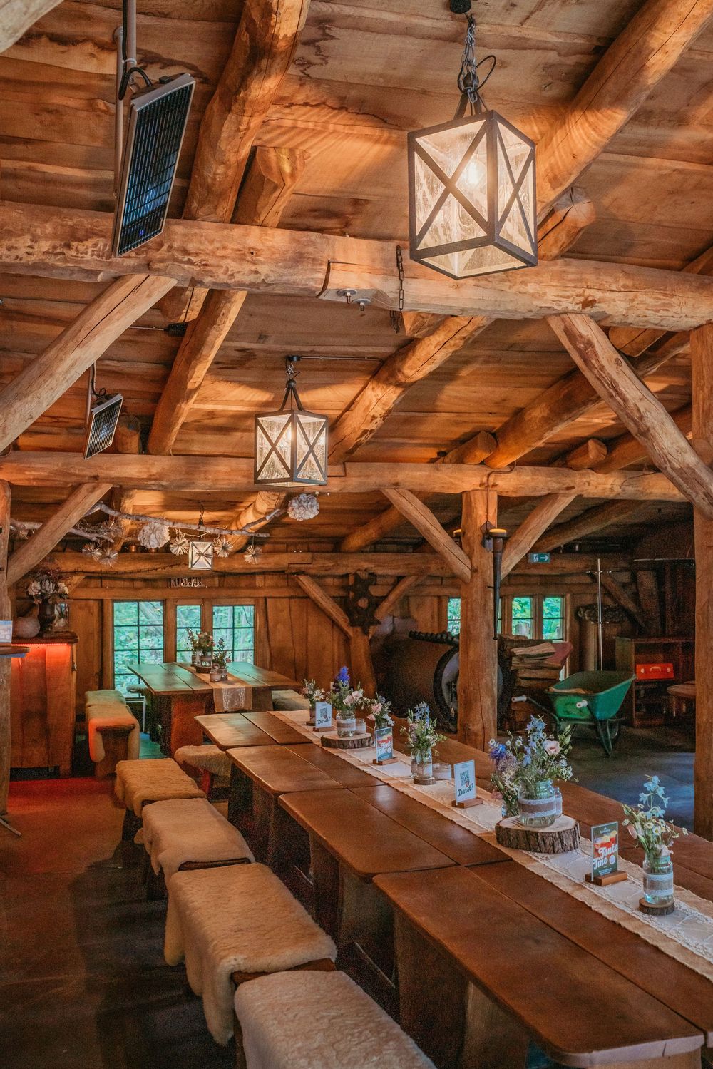 Rustic timber-framed barn interior with long wooden tables and hanging lanterns set up for dining or events.