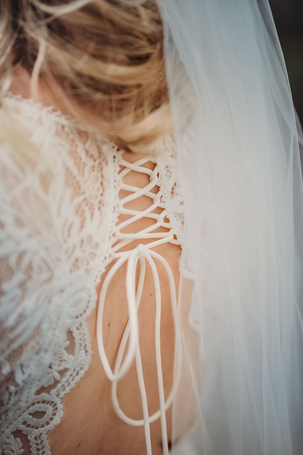 Close-up details of a white corset-style wedding dress back with delicate lace overlay and satin ribbon lacing.