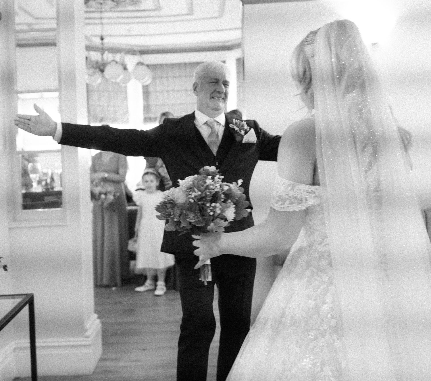 Black and white photo of a joyful moment during a wedding ceremony with a bride in white lace dress holding a bouquet.