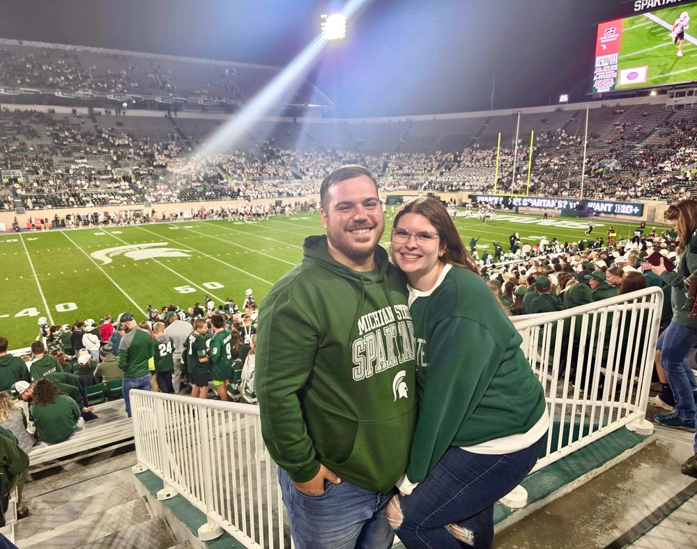 Spectators wearing green jerseys watch from stadium seats at a sporting event.