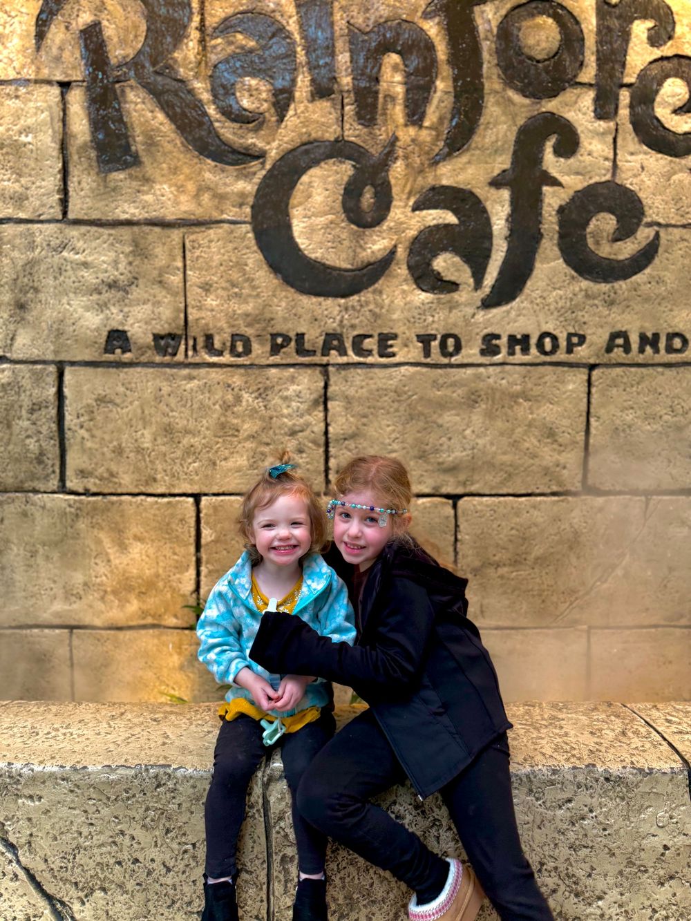 Two people pose together against a vintage stone wall with decorative text signage.