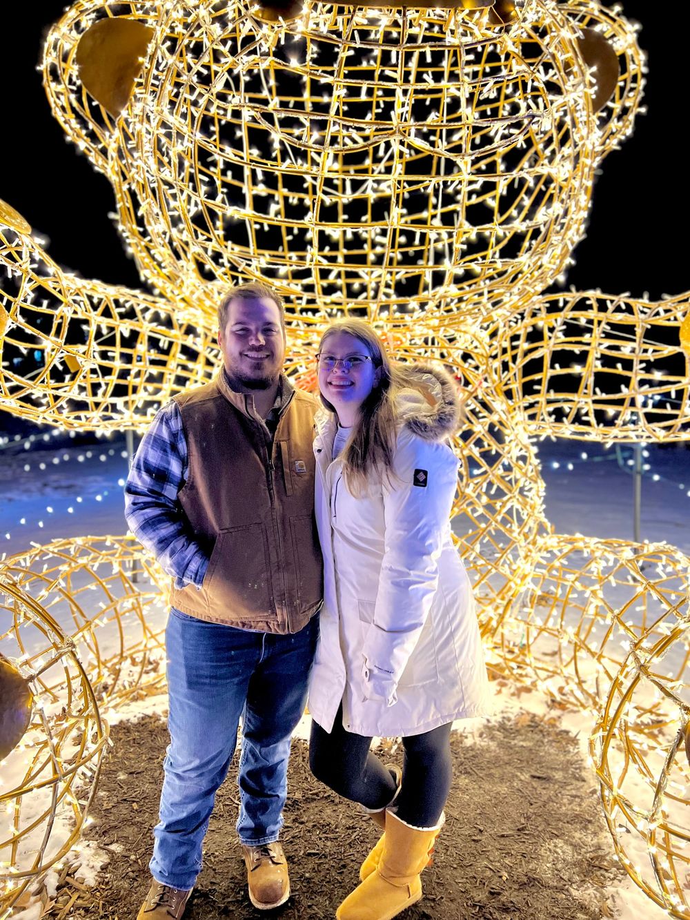 People posing in front of large illuminated holiday light displays at night.