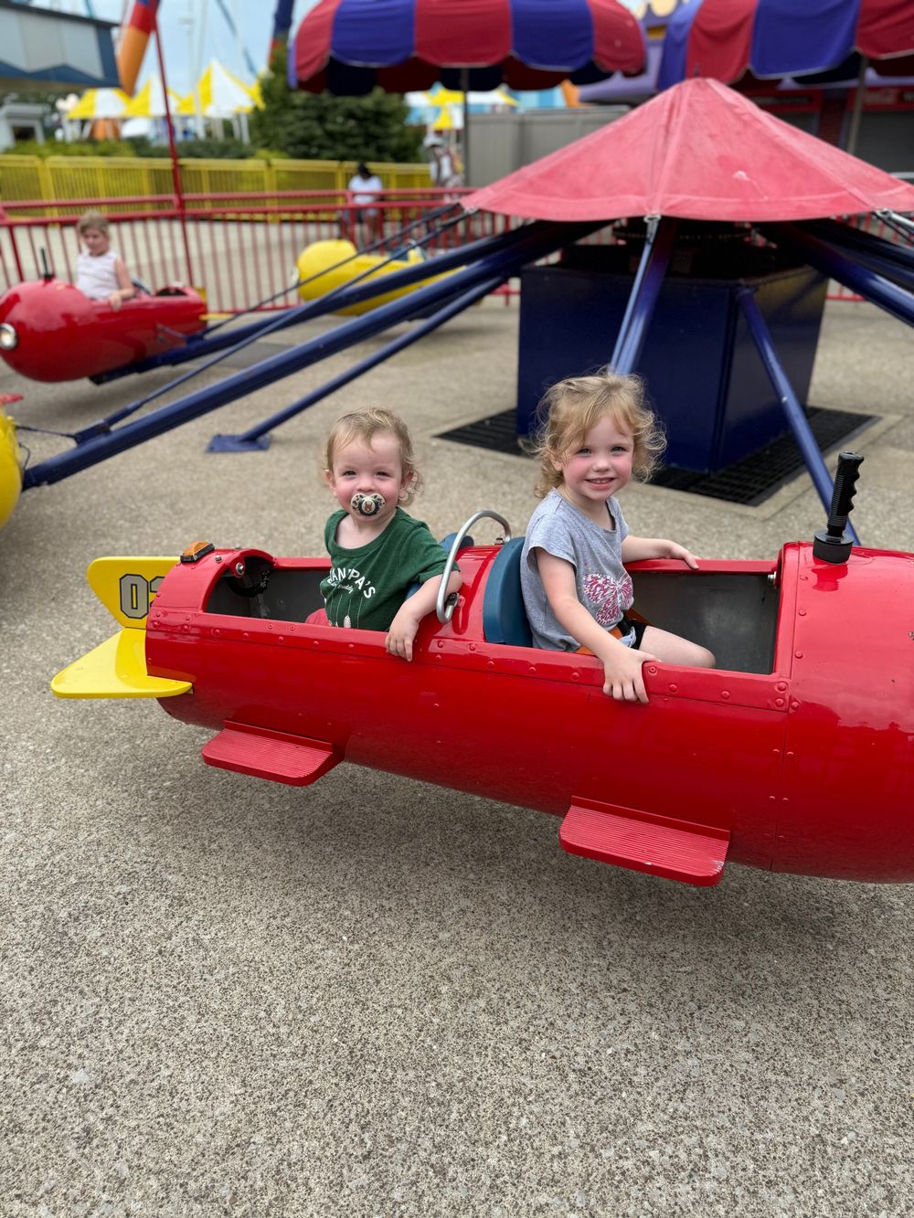 Kids enjoying a red carnival ride at an outdoor fair.