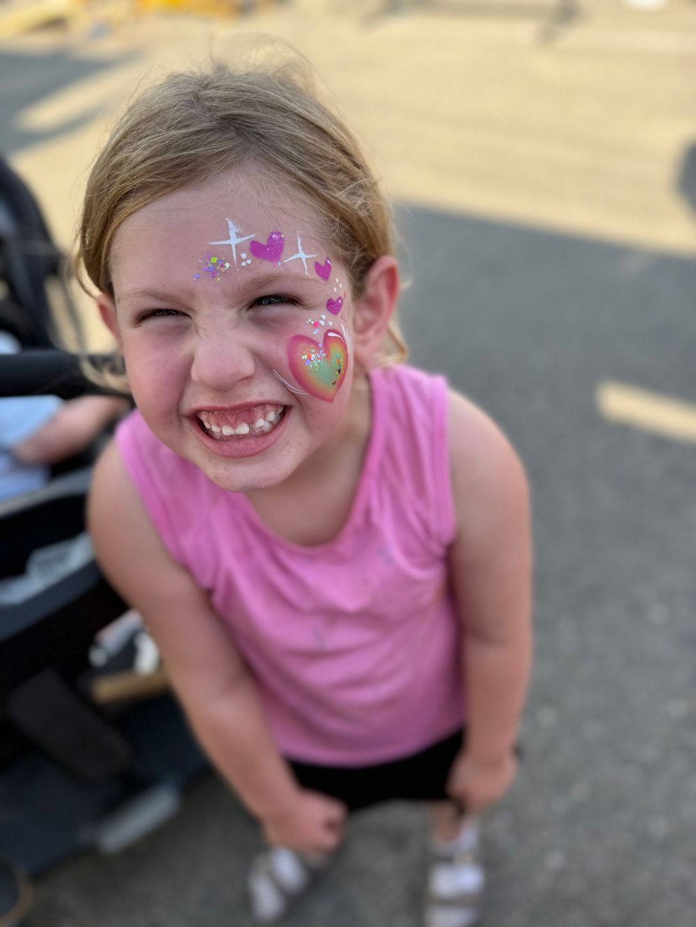 Child wearing face paint and pink shirt at outdoor event.