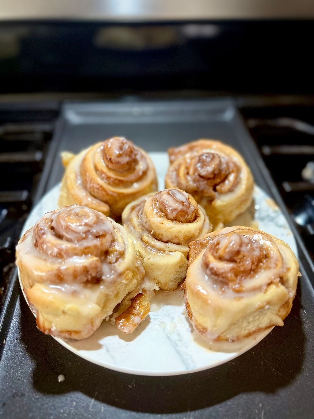 Freshly baked cinnamon rolls with vanilla glaze cooling on a plate.