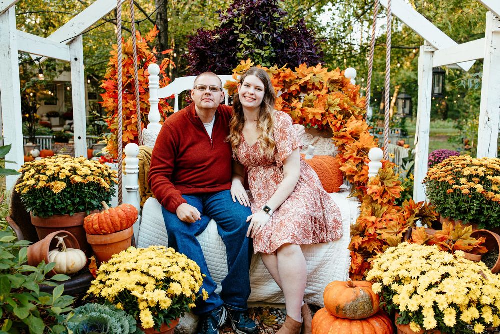 Autumn scene with white pergola decorated with pumpkins, mums, and fall foliage.