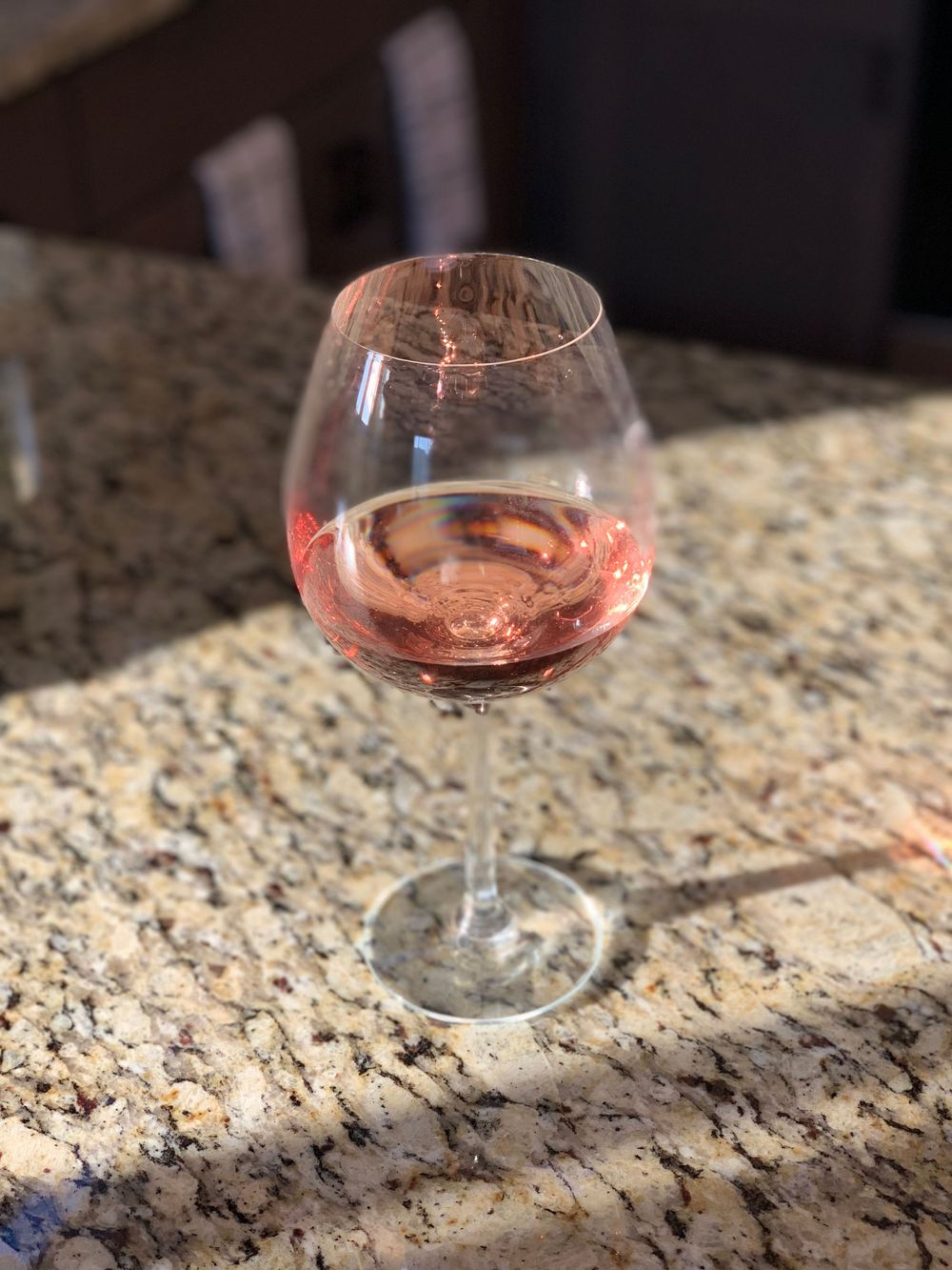A glass of rosé wine catching sunlight on a granite countertop.