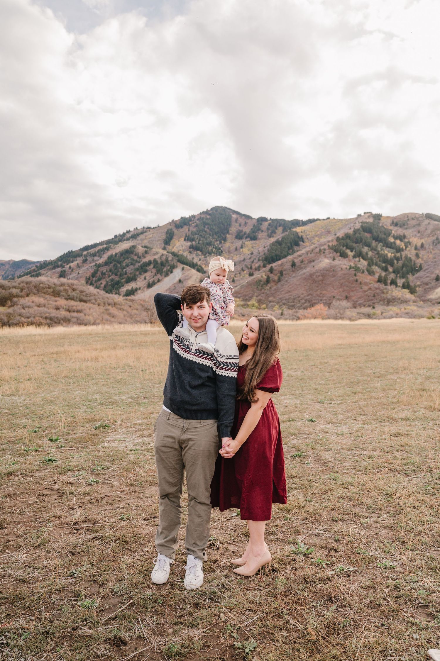 A couple shares a playful moment together in a field with mountains in the background.