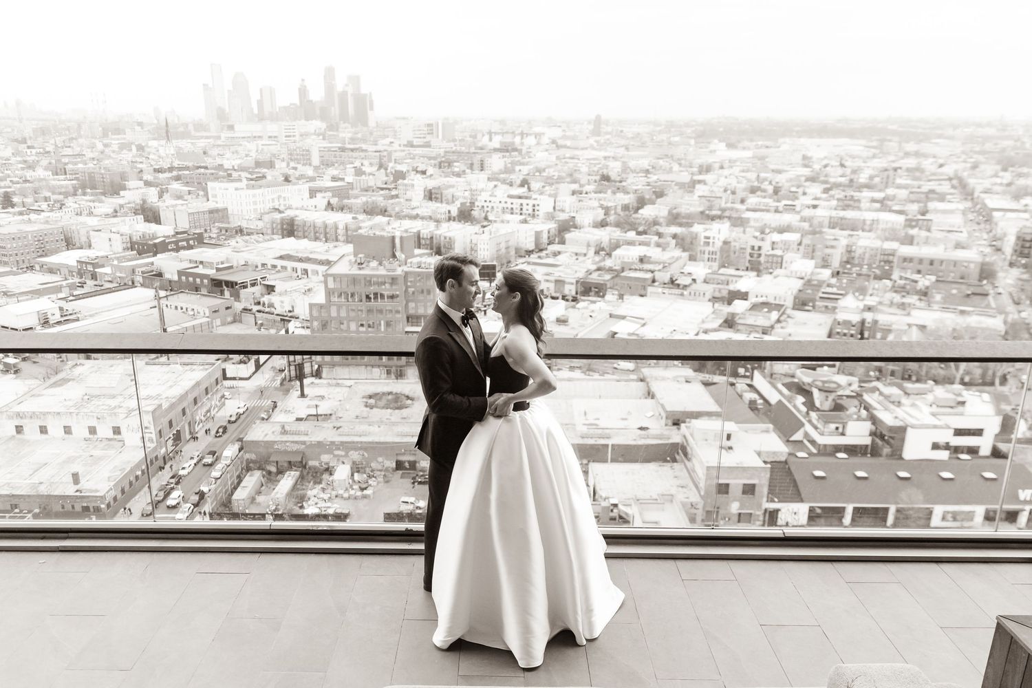 A black and white urban wedding photo with tall buildings and people on a city street.