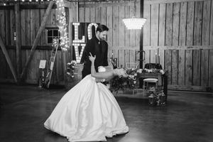 Bride and groom share romantic first dance dip in rustic barn wedding venue with LOVE marquee lights.