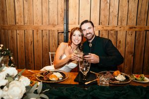 Bride and groom smiling and toasting champagne at sweetheart table with green velvet runner at wedding reception.