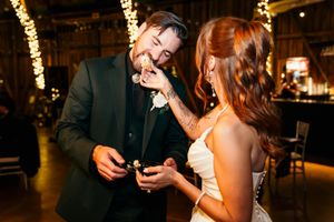 Bride and groom share cake cutting moment in warmly lit barn wedding reception venue.