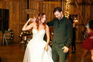 Bride and groom share a joyful first dance in a warmly lit rustic barn wedding reception.
