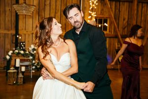 Bride and groom share an intimate dance in a rustic barn wedding venue with warm string lights.
