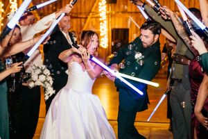 Bride and groom duel with lightsabers during Star Wars themed wedding reception exit with guests.