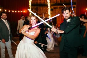 Bride and groom playfully dueling with colorful lightsabers at their Star Wars themed wedding reception.