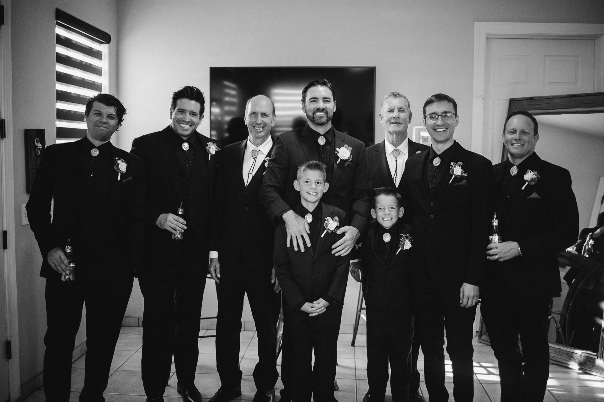 Black and white photo of groomsmen and ring bearer in suits with boutonnieres posing together before a wedding ceremony.