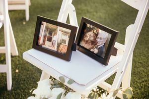 Two framed photos displayed on a white chair as memorial decor at an outdoor wedding ceremony.