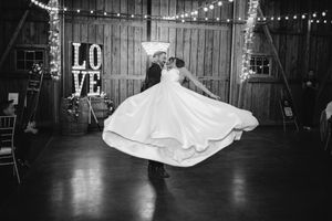 Black and white photo of groom spinning bride on dance floor with LOVE sign backdrop.