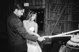 Bride and groom cut wedding cake with a lightsaber in black and white barn reception photo.