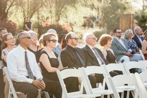 Wedding guests seated in white chairs at an outdoor ceremony on a sunny day.