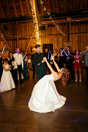 Bride and groom share first dance with lightsabers in rustic barn wedding reception.
