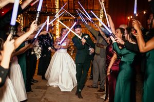 Bride and groom walk through a lightsaber tunnel held by guests during a Star Wars themed wedding reception.